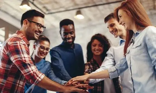 A diverse group of smiling young professionals joining hands.