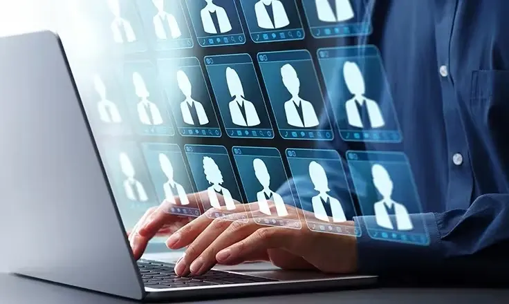 A person in a blue shirt types on a laptop as numerous holographic profile icons float above the keyboard.