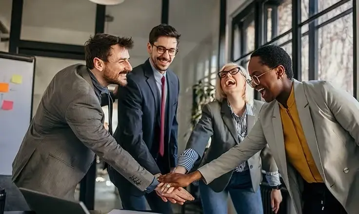 A group of cheerful business colleagues, laughing with their hands joined, in a modern office.