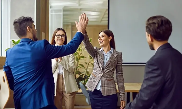 A group of professionals smiling and giving each other a high five in a bright, modern office setting.