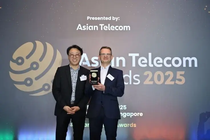 Two professionals posing for a photo at the Asian Telecom Awards 2025, with one individual holding a trophy in front of a branded backdrop.