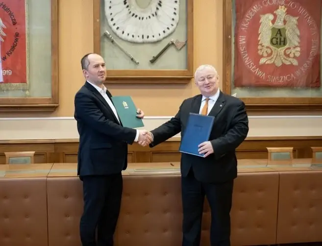 Marcin Kaleta and Rafał Wiśniowski shaking hands and holding folders at the AGH University of Science and Technology in Kraków.