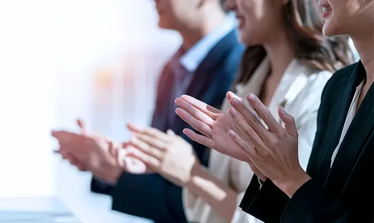A group of business professionals in formal attire sitting in a row and clapping.