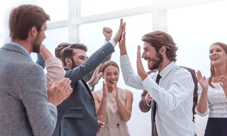 A group of office workers giving high fives and clapping during a celebration in a bright office.