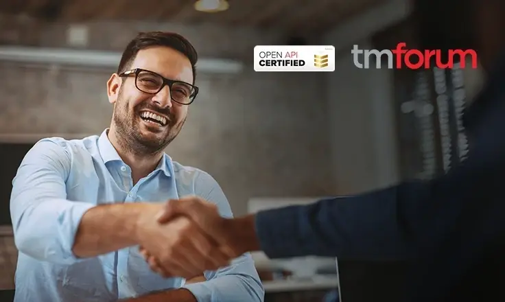 A man in a light blue shirt, laughing, shaking hands with someone off-camera, overlaid with the "TM Forum" and "Open API Certified" logos.