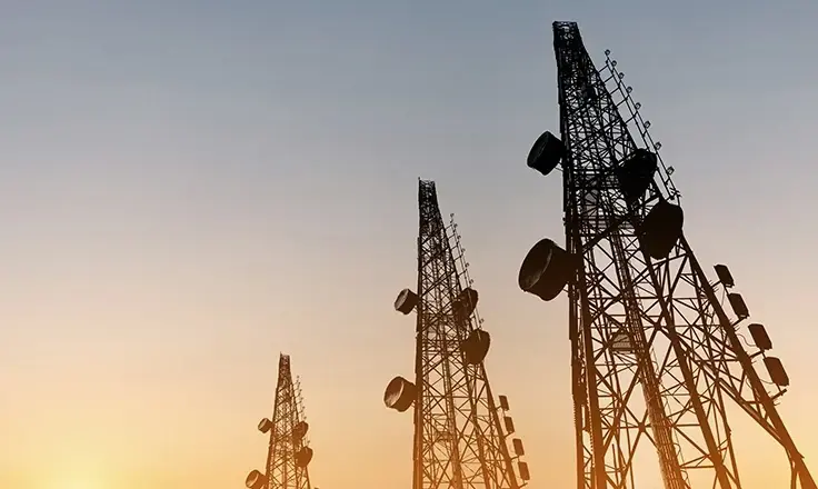Silhouette of three large telecommunication towers standing against a warm sunset sky.