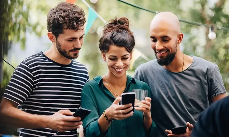 Three friends smiling and looking at a smartphone together.