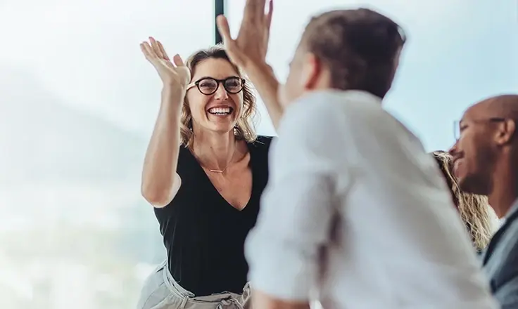 A group of colleagues celebrating and high-fiving during an office meeting.