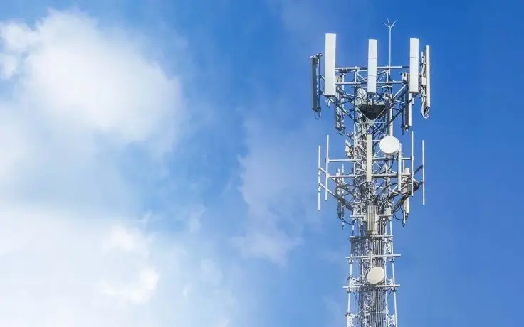 A white communications tower with multiple antennas against a bright blue sky with white clouds.