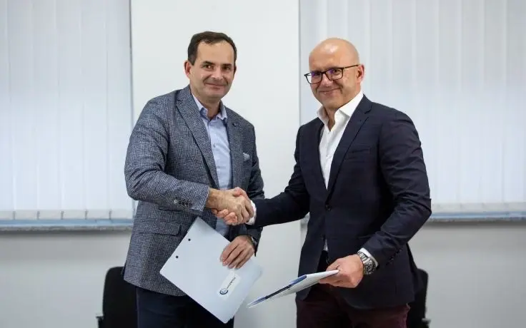 Sławomir Pietrzyk and Jacek Lonc smiling and shaking hands while holding folders in an office setting.