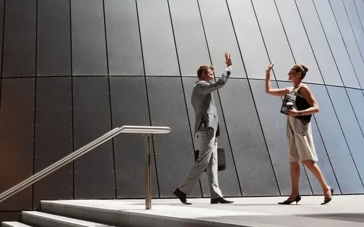 Two business professionals in formal attire giving each other a high five outside a modern building with a curved facade.