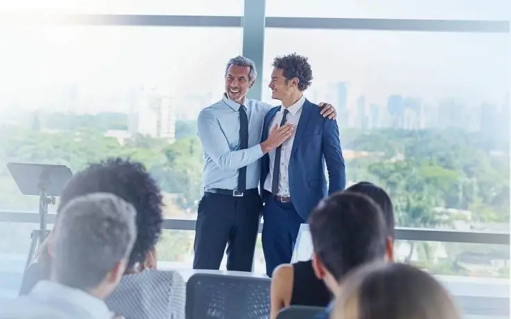 Senior executive praising a young professional during a business presentation in a modern office with a city view.