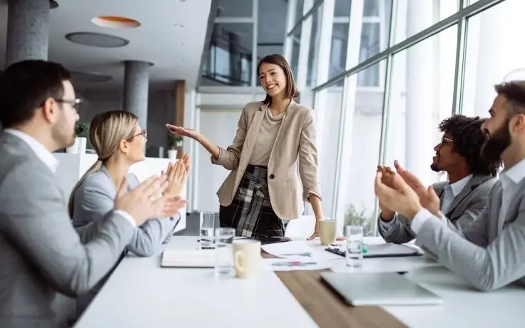 A diverse team of business professionals clapping and cheering for a colleague during an office meeting.