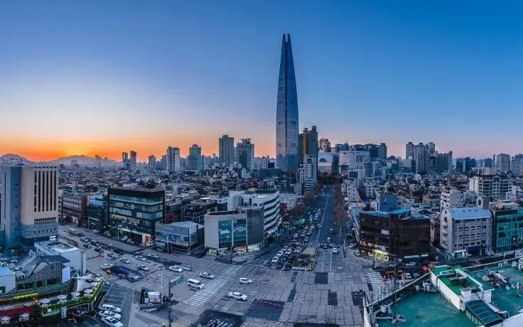 Wide-angle city panorama at sunset featuring the Lotte World Tower skyscraper rising above the Seoul skyline.