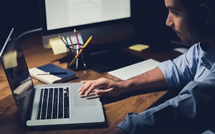 An office worker working on a laptop in a dark office.