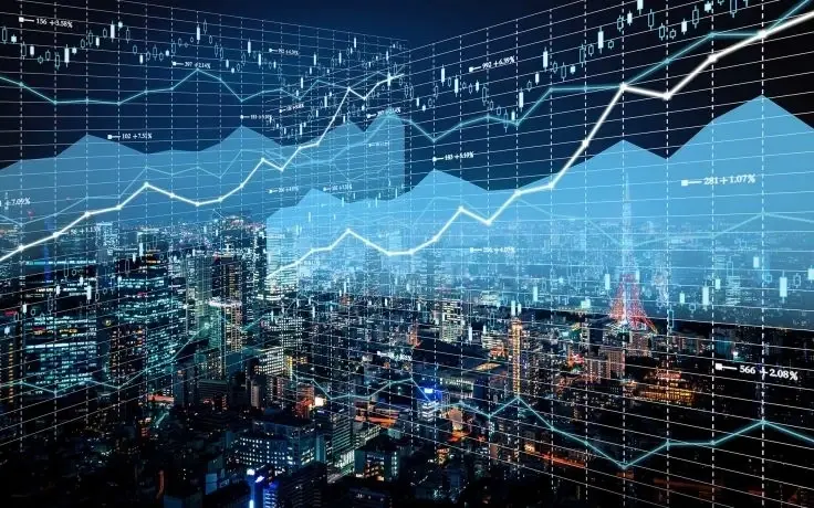A nighttime aerial view of a brightly lit city skyline overlaid with glowing financial charts and line graphs.