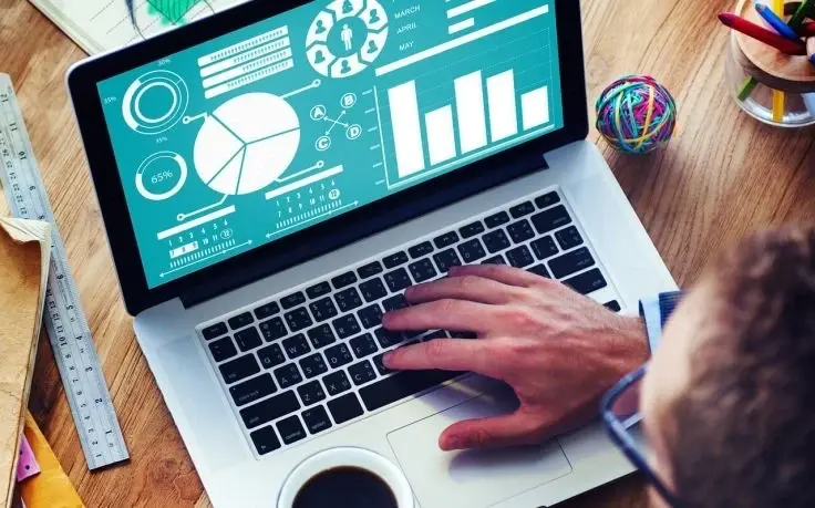 High-angle view of a person using a laptop displaying white data charts and graphs on a teal background.