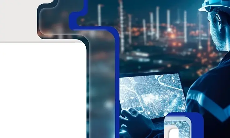 An industrial worker in a hard hat uses a laptop showing a digital map against a blurred factory background at night.