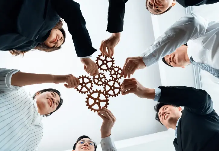 Low-angle view of a team of smiling professionals in business attire, putting together interlocking wooden gears.