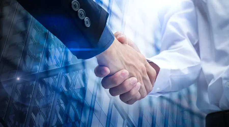 Two people in business attire shaking hands, with a double-exposure effect showing a modern glass office building.