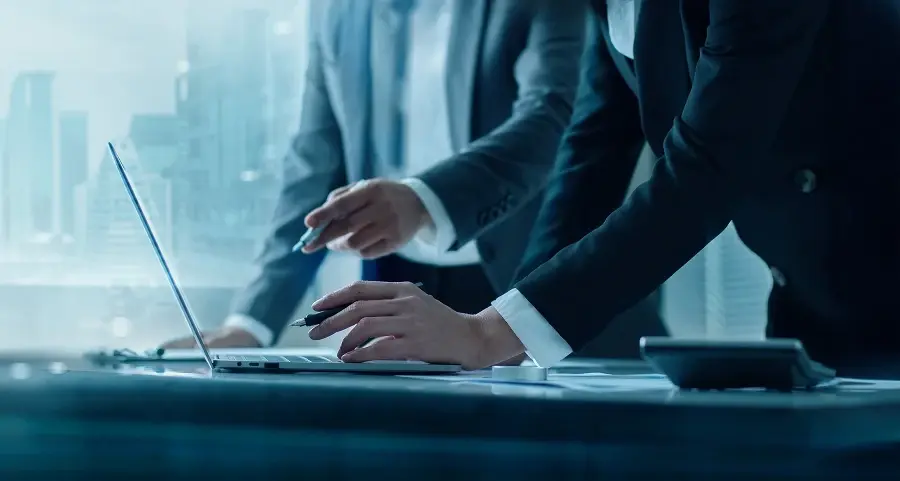 Two professionals in business attire at a desk with a laptop and documents, viewed from a low angle.