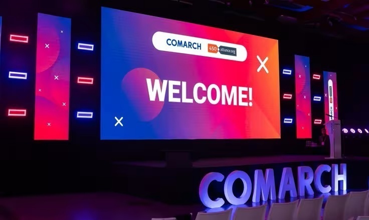 A large "WELCOME!" screen for a Comarch event on a stage with colorful lighting and "COMARCH" in large letters in front.
