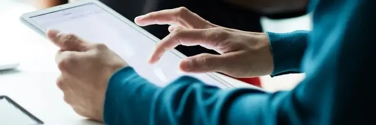A close-up of a person's hands holding and interacting with the touchscreen of a white digital tablet.